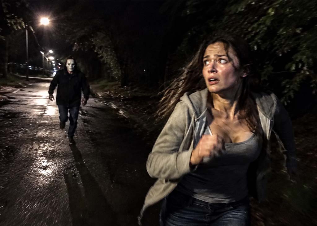 Night scene on a dark street featuring a woman running away from masked man behind her.